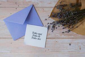POSITIVE MIND LIFE VIBES text on supportive message paper note reminder from violet envelope. Flat lay composition dry lavender flowers. Concept of inner happiness, slowing-down digital detox personal fulfillment. Top view photo