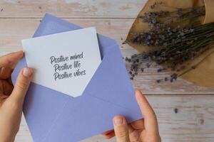 Female hands taking paper card note with text POSITIVE MIND LIFE VIBES from violet envelope. Lavender flower. Top view, flat lay. Concept of mental spiritual health self care wellbeing mindfulness photo