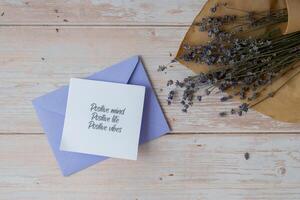 Female hands taking paper card note with text POSITIVE MIND LIFE VIBES from violet envelope. Lavender flower. Top view, flat lay. Concept of mental spiritual health self care wellbeing mindfulness photo