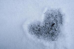 Heart shape love sign is drawn in snowy glade romantic background. Valentine's Day cold heart in snow winter season weather. Outdoor concept photo