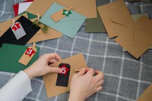 Number on craft envelopes notes with tasks before Christmas holidays. Female making kraft paper for handmade advent calendar Made with your own hands step by step DIY crafts do it yourself photo