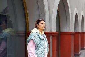 Woman in quilted jacket strolling by arched architecture photo