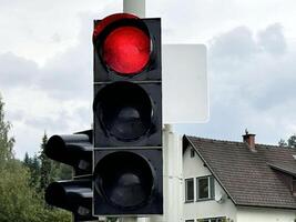 Red traffic light at intersection on cloudy day with empty street in background photo