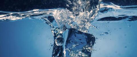 Water splashing and ice cube. Ice splashing into a glass of water. Underwater pouring ice cubes falling into clear watering background. Refreshing chill drinking. Ices in a glass with blue background photo