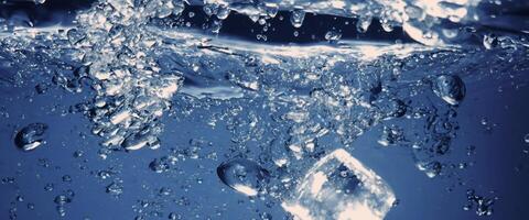 Water splashing and ice cube. Ice splashing into a glass of water. Underwater pouring ice cubes falling into clear watering background. Refreshing chill drinking. Ices in a glass with blue background photo