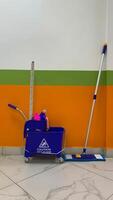 Blue trolley cleaning bucket with mop and cleaning products in corridor, vertical photography of floor cleaning service concept, cleaning bucket on wheels with inscription caution wet floor photo