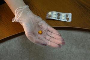 Hand in medical glove holds expired tablet brown color against background of plate of tablets that have lost their expiration date, monitoring suitability and freshness of medicaments photo