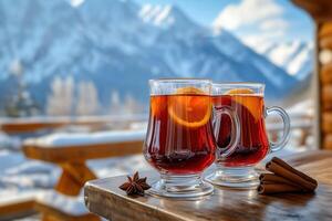 Two glasses of red mulled wine. Hot winter drink with cinnamon, cardamom, orange, anise on a village table against the backdrop of snow-capped mountains photo