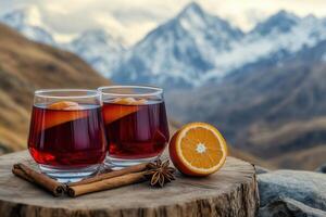Two glasses of red mulled wine. Hot winter drink with cinnamon, cardamom, orange, anise on a village table against the backdrop of snow-capped mountains photo