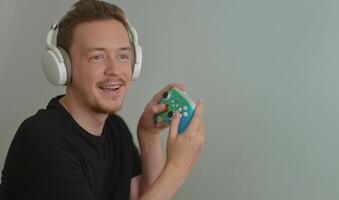 A young man wearing headphones playing game by Console Controller. Gamer with joystick smiling after win. Happiness, delight and joy emotion concept. Banner background with copy space photo