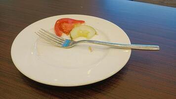 Empty plate with a fork, tomato and cucumber slices on a wooden table. photo