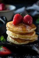 A stack of four golden brown pancakes topped with fresh strawberries and a drizzle of maple syrup. photo