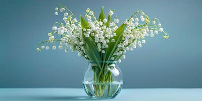 A bouquet of lily of the valley flowers in a glass vase on a blue background. photo