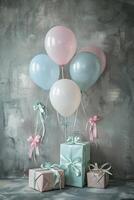 Four pastel-colored balloons with pink and blue ribbons attached float over three wrapped gifts against a gray concrete wall. photo