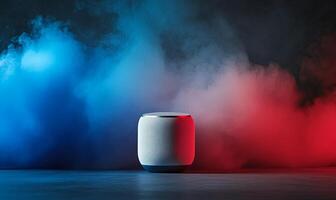 A silver, round, cylindrical speaker with a black base sits on a dark, concrete surface against a background of blue and red smoke. photo