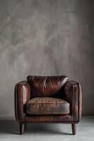 A brown leather armchair with wooden legs sits in front of a grey textured wall. photo
