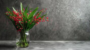 A bouquet of red berries and green leaves in a glass vase against a gray background. photo