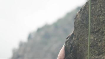 A climber reaches for a foothold on a rocky cliff while scaling a challenging route in a dramatic outdoor landscape video