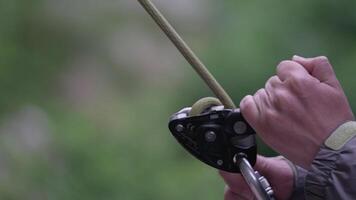 A climber hands gripping a belay device while preparing for an ascent in a lush green outdoor environment during daylight hours video