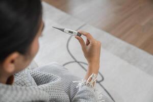 Woman Checking Her Temperature with a Digital Thermometer While Feeling Unwell at Home photo