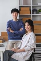 Young Couple Running a Small Online Business from Home, Surrounded by Shipping Boxes and Office Supplies, Smiling and Confident in Their Modern Workspace photo