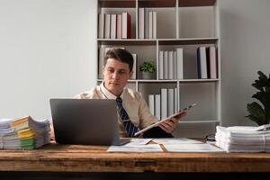 Young Businessman Working in Modern Office with Laptop and Documents, Focused on Tasks, Professional Workspace photo