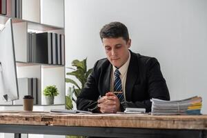 Young Businessman Deep in Thought at Modern Office Desk with Documents and Computer, Focused on Serious Work photo