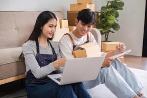 Young Couple Preparing Merchandise for Online Delivery While Checking Boxes and Using Laptop photo