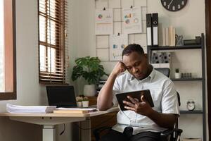 American Businessman Feeling Tired and Overworked While Sitting at Desk in Modern Office with Tablet and Documents photo
