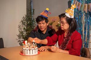 A man and woman are sitting at a table with a birthday cake in front of them photo