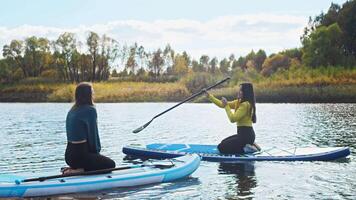 start of sap surfing training. coach explains to girl how to properly control paddleboarding board with the help of paddle on water. Slow motion video