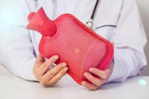 The doctor is holding a red heating pad with hot water in his hands. The concept of heat treatment, muscle relaxation, spasm relief, close-up photo