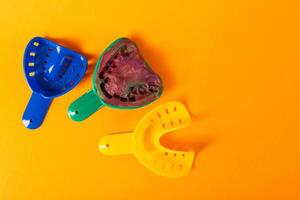Multi-colored dental spoons for taking an impression of the dental jaw on a orange background. Making an impression of the jaw for braces and dental prosthetics, close-up. Copy space for text photo