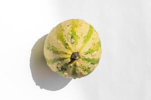 A small, round yellow and green gourd on a white background, representing autumn harvest and Thanksgiving decoration themes photo