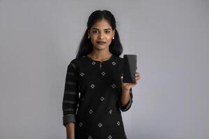 Young beautiful woman holding and showing blank screen of smartphone or mobile or tablet phone on a gray background. photo