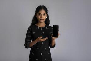 Young beautiful woman holding and showing blank screen of smartphone or mobile or tablet phone on a gray background. photo