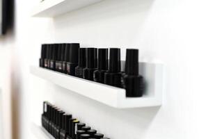 Shelves display rows of black nail polish bottles in a minimalist style. Beauty and fashion photo