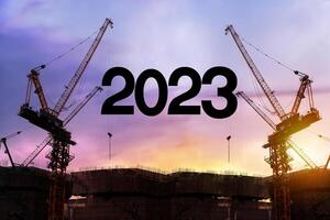 Businessman engineer looking 2023 blueprint in a building site. Silhouette of construction worker with crane and cloudy sky for preparation of welcome 2023 new year photo