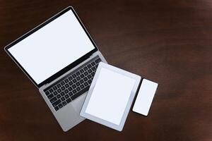 Laptops, tablets and smartphones with blank screens on table, devices are highly used in communication technology these days. Flat top view with copy space photo