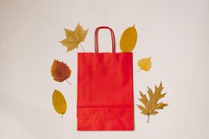 Autumn flat lay. A craft red bag and autumn fallen leaves side by side on a light background. Autumn concept of discounts and sales photo