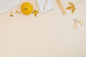 Flat lay home office desk. Freelancer or blogger workplace with computer, yellow pumpkins, fallen leaves, scissors, notepad, ruler and pen on a light beige background with copy space photo