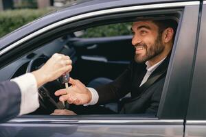 Close up of smiling business man in suit receiving car keys to new vehicle photo