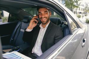 Smiling businessman talking phone with client while sitting on car backseats photo