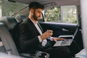 Businessman working on laptop sitting car backseat on the way to office and drinking coffee photo