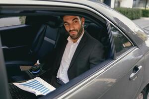 Confidence businessman sitting on car backseat and working with documents and use laptop photo