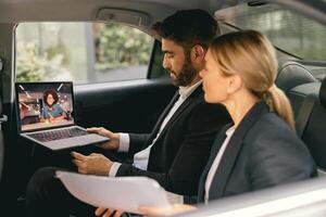 Smiling business people have online meeting using laptop while sitting in car back seats photo