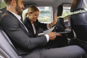 Cheerful business people have online meeting using laptop while sitting in car back seats photo