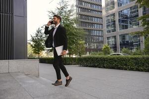Handsome businessman talking by mobile phone standing on background of modern building photo
