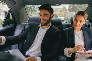 Smiling business analysts have online meeting using laptop while sitting in car back seats photo