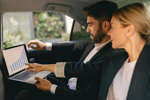 Successful business analysts couple working together use laptop in back seat of car photo